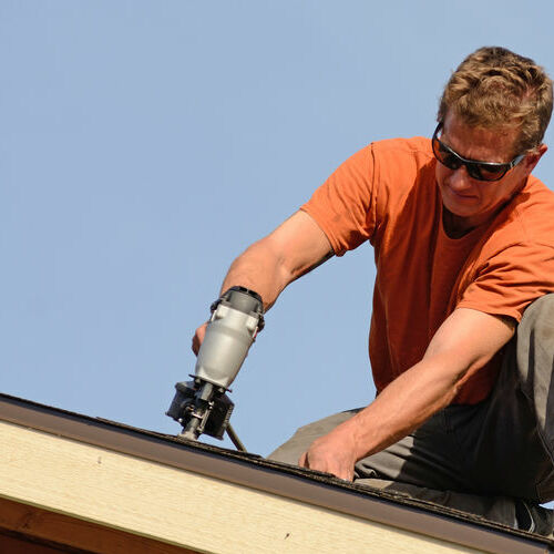 A Roofer Nails in Shingles.
